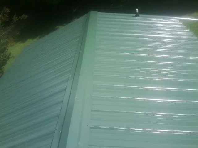 New green metal panels meeting at the ridge of a roof — Flat Roof Repair work by our crew in Wilmington
